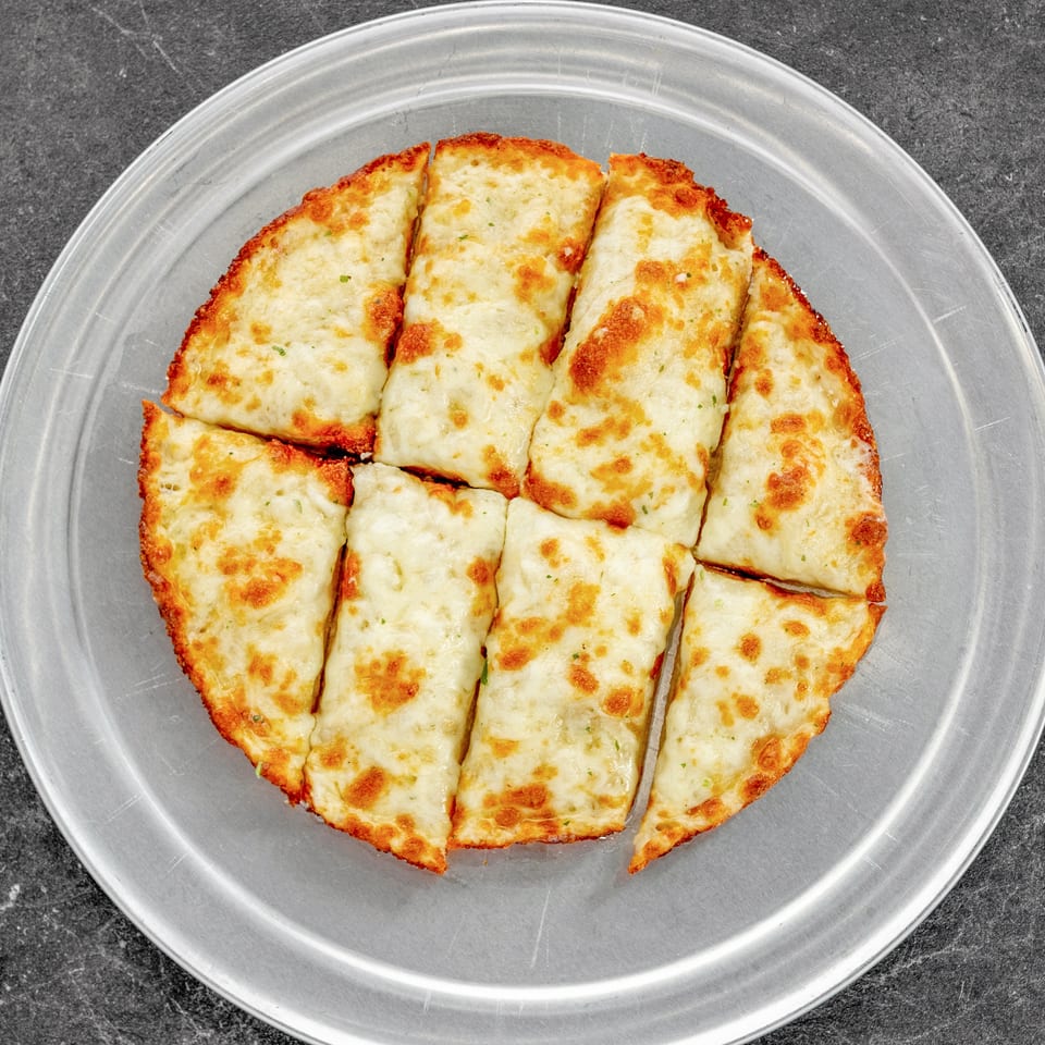 Golden-brown cheesy breadsticks arranged on a clear plate over a dark countertop.