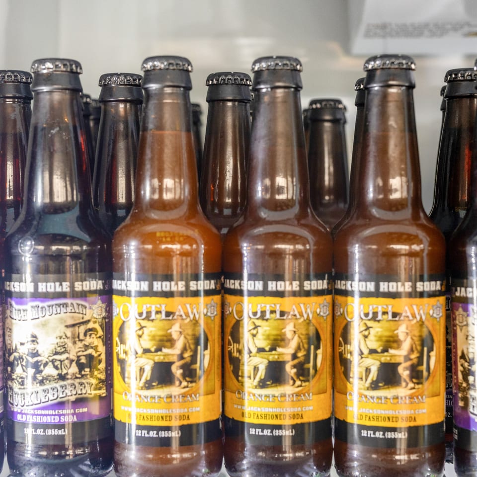 Rows of bottled Jackson Hole Soda in orange cream and huckleberry flavors displayed on a shelf.