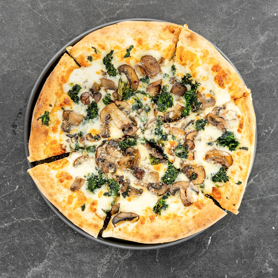 Sliced cheese pizza topped with mushrooms and leafy greens on a black plate against a dark stone surface.