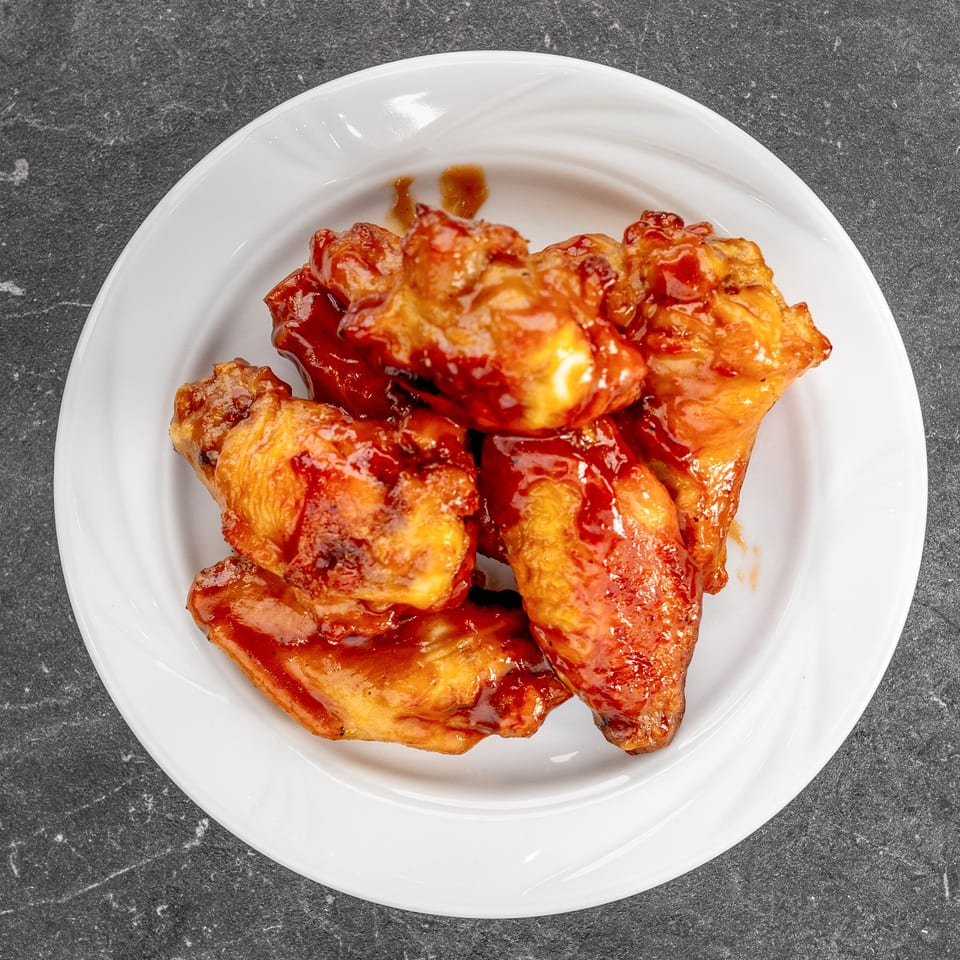 Crispy fried chicken pieces glazed with red sauce on a white plate atop a dark stone countertop.
