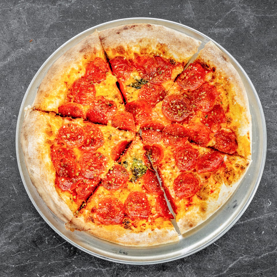 Overhead view of a sliced pepperoni pizza with melted cheese and herbs on a metal tray.