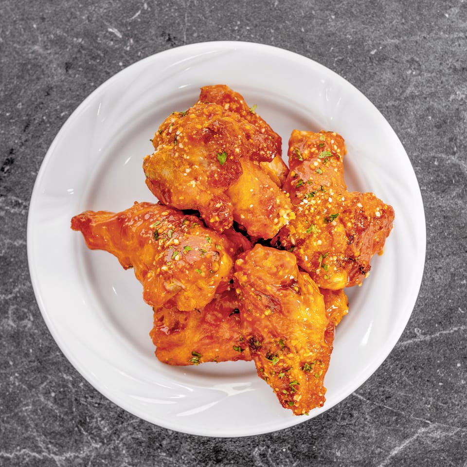 Plate of crispy chicken wings coated in orange sauce, sprinkled with minced garlic and green herbs.